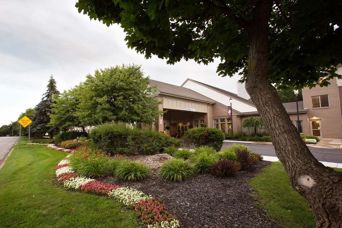A building entrance surrounded by lush landscaping, featuring a variety of trees and colorful flowers.