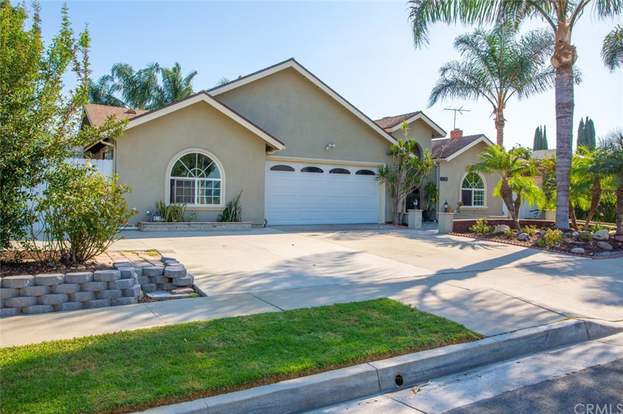 A suburban house with a neatly landscaped front yard and palm trees.