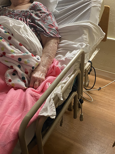 A patient's arm resting on the edge of a hospital bed, surrounded by blankets.