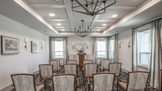 A well-lit room with arranged chairs facing a podium and decorative chandeliers.