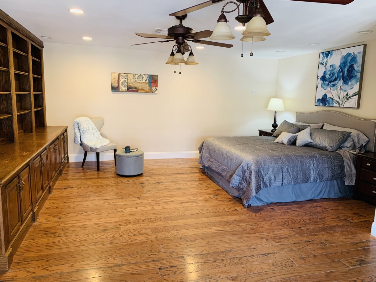 A modern bedroom featuring a king-sized bed with gray bedding, hardwood flooring, and stylish decor elements.