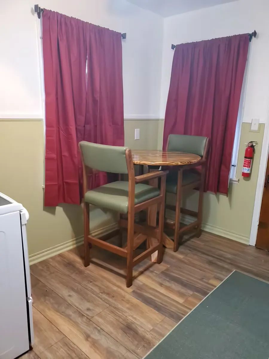 A small room with a wooden high table and two chairs, near red curtains and a light green wall.