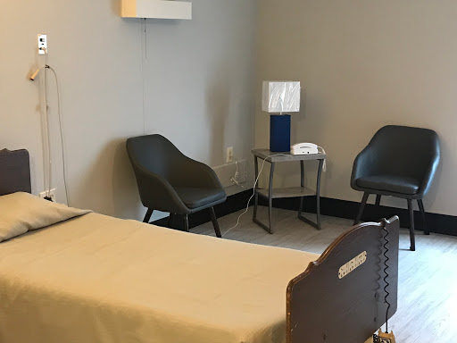 A simple and modern room featuring a bed, two chairs, and a lamp.