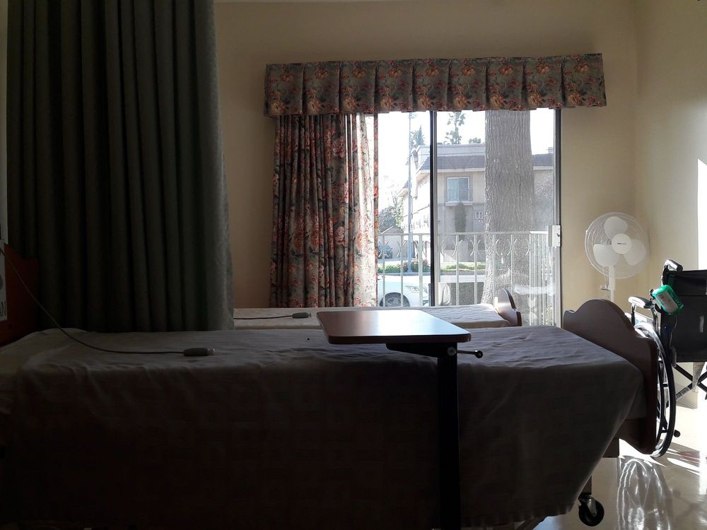 A hospital room with a bed, curtains, and sunlight streaming through a window.