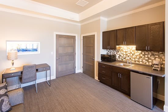 A modern kitchenette with dark cabinetry and a small desk area in a neutrally colored room.