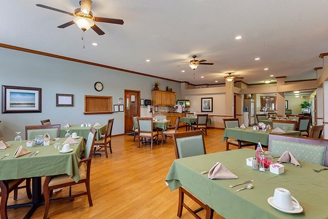 A spacious dining area with tables set for guests, featuring wooden floors and ceiling fans.
