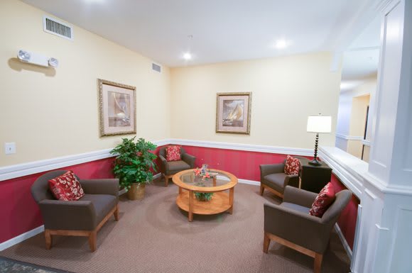 A cozy waiting room with a seating area, featuring four chairs, a round coffee table, wall art, and a potted plant.