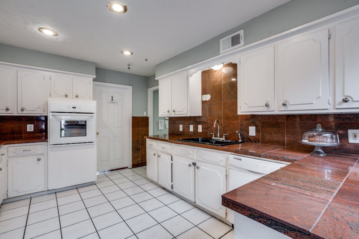 A modern kitchen featuring white cabinets, a built-in oven, and a double sink with a tiled floor.