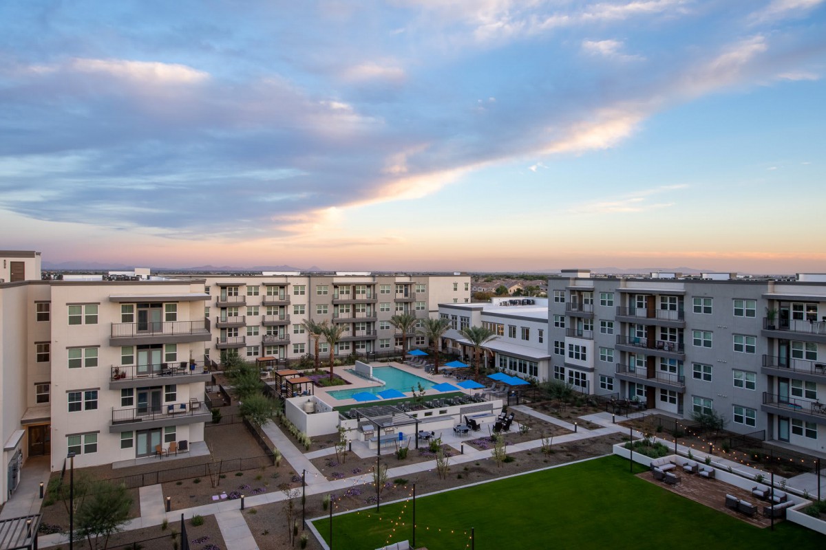 A modern apartment complex featuring a central swimming pool at sunset.