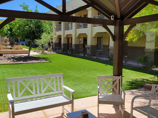 A serene outdoor patio area with white furniture, overlooking a manicured lawn and sunny surroundings.