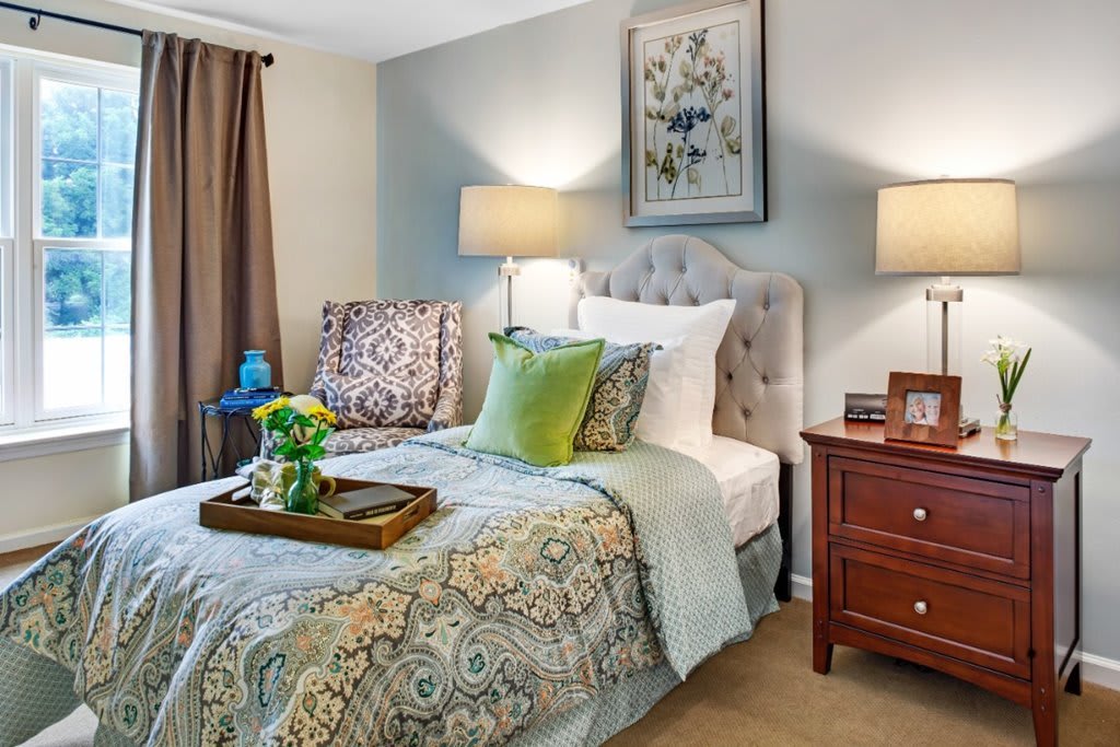 A cozy bedroom featuring a neatly made bed with patterned bedding, decorative pillows, and a wooden nightstand with lamps.