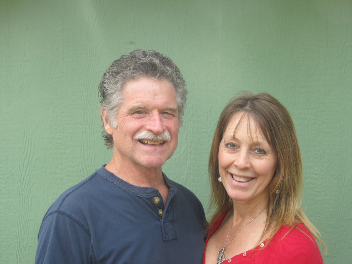 A smiling couple standing together in front of a green background.