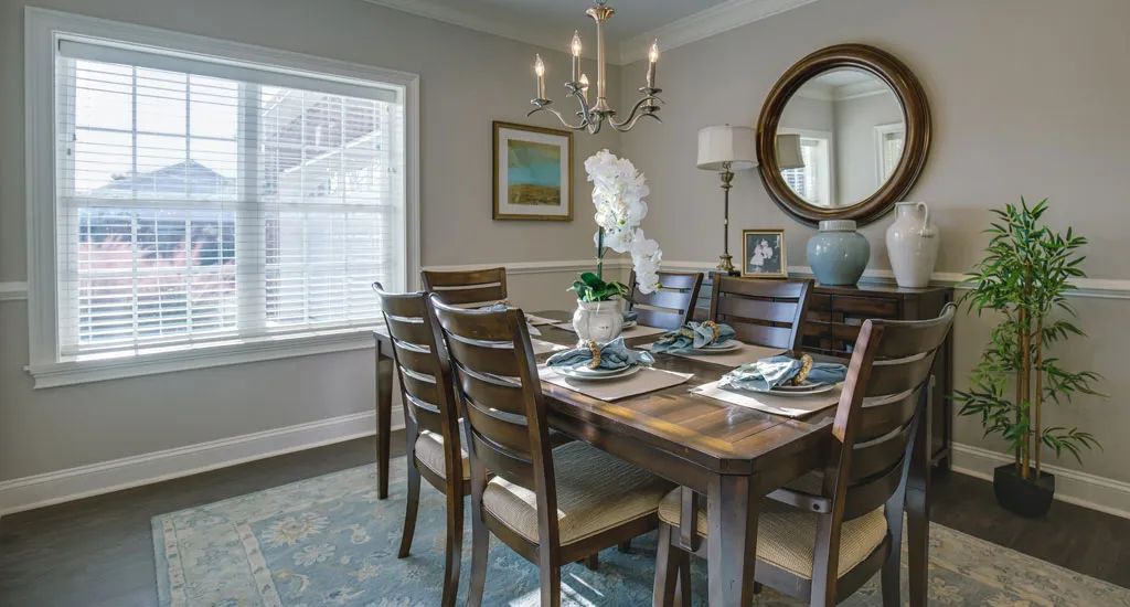 A cozy dining room with a wooden table set, decorative mirror, and chandelier.