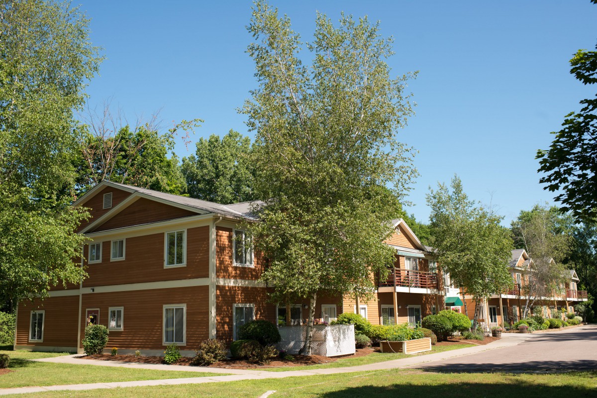 A two-story apartment building surrounded by trees on a sunny day.