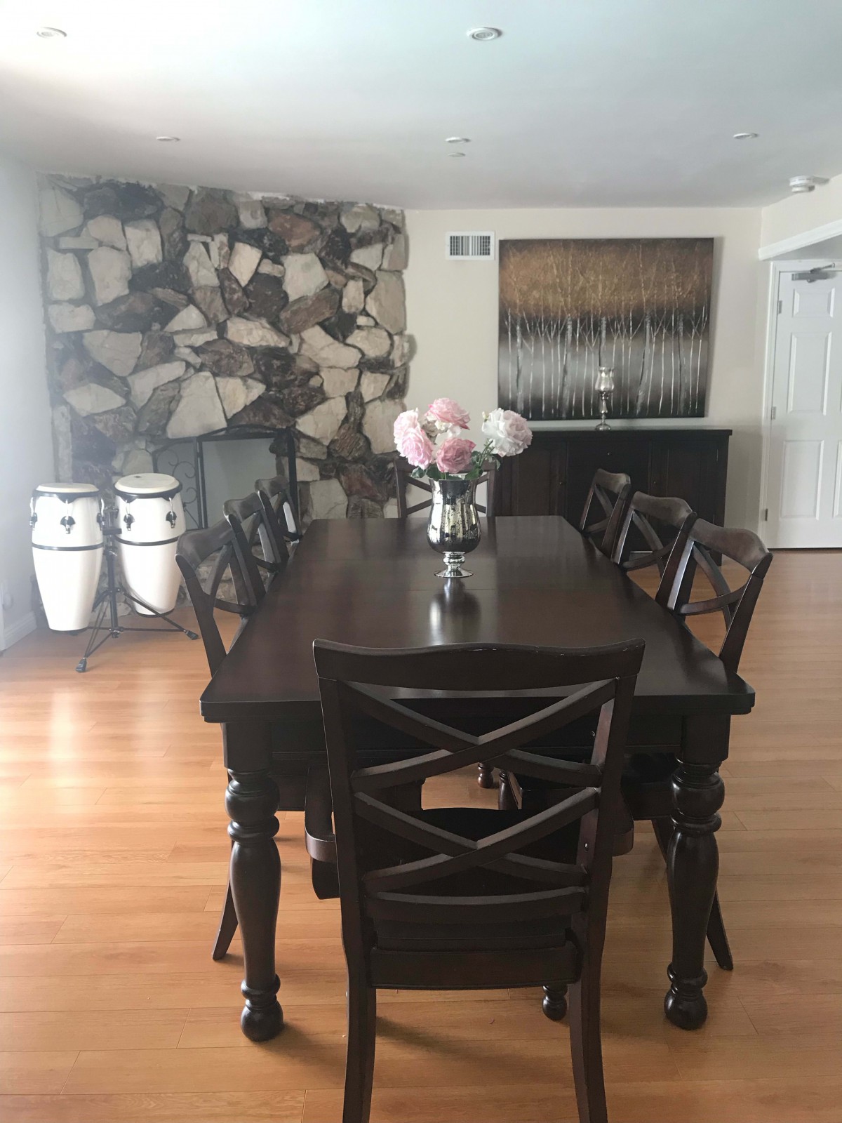 A modern dining room with a dark wood table, chairs, and decorative elements including flowers and conga drums.