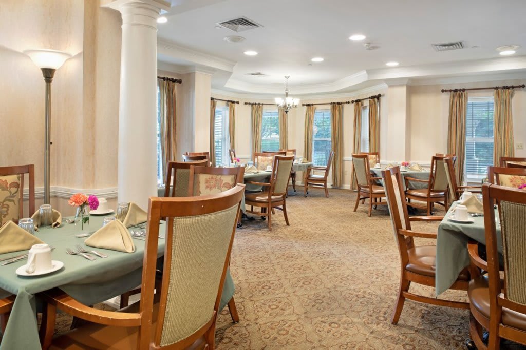 A well-furnished dining area with elegant tables and chairs, featuring warm lighting and a carpeted floor.