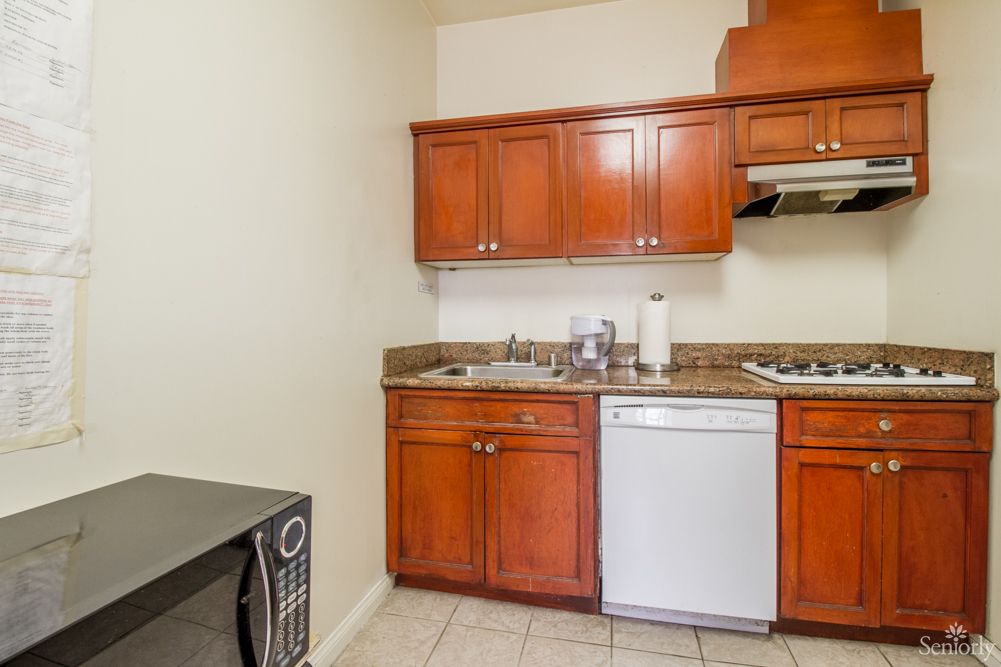 A compact kitchen area with wooden cabinets, a sink, a dishwasher, and a microwave.