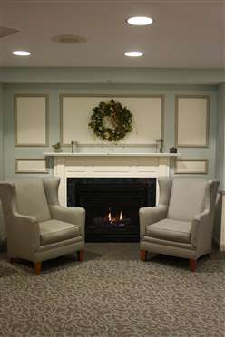 A cozy living room with a fireplace, two chairs, and a decorative wreath above the mantel.