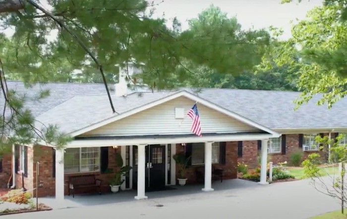 A house with a covered entrance displaying an American flag, surrounded by trees.