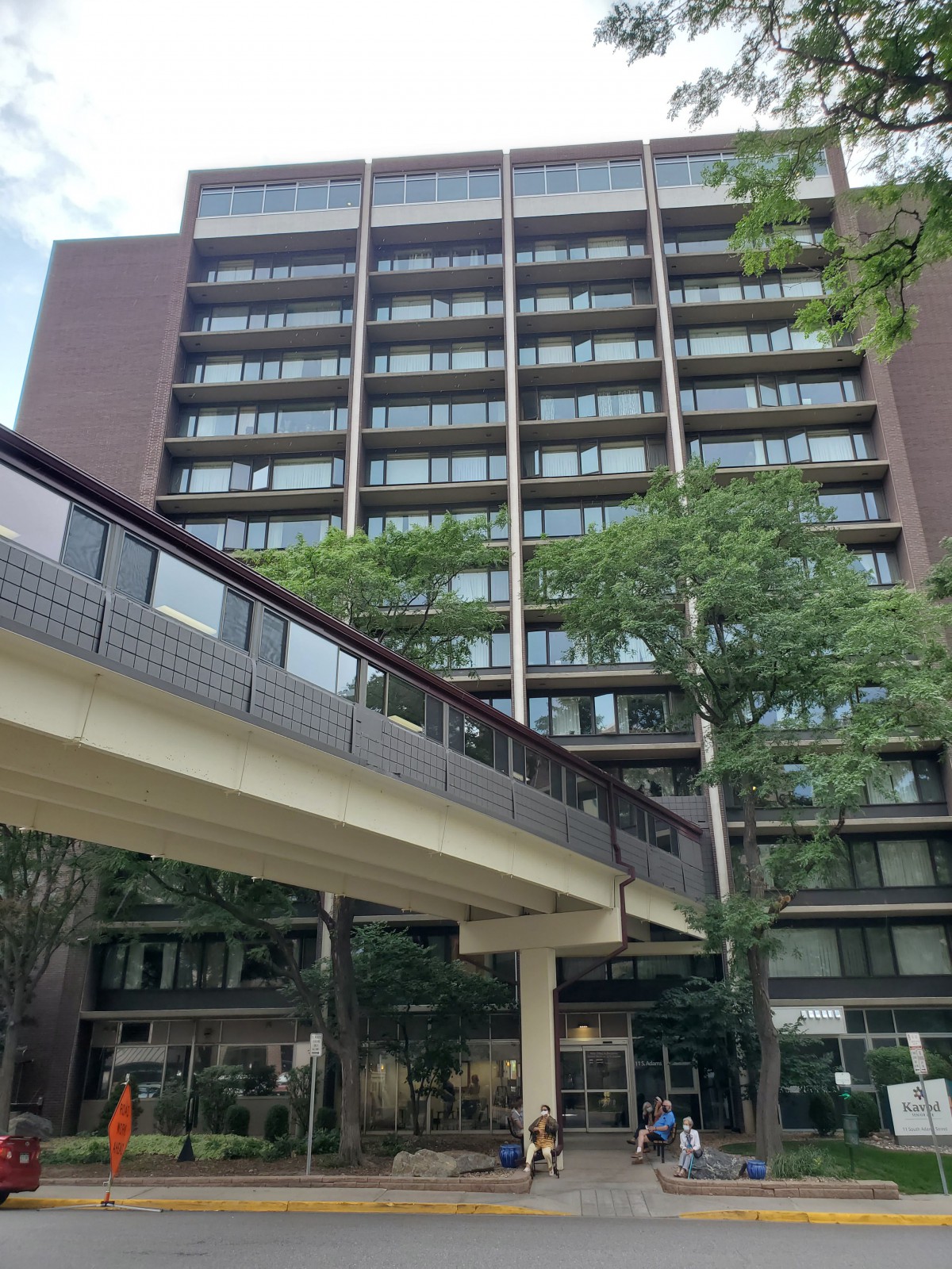 A modern multi-story building with a skywalk surrounded by trees.