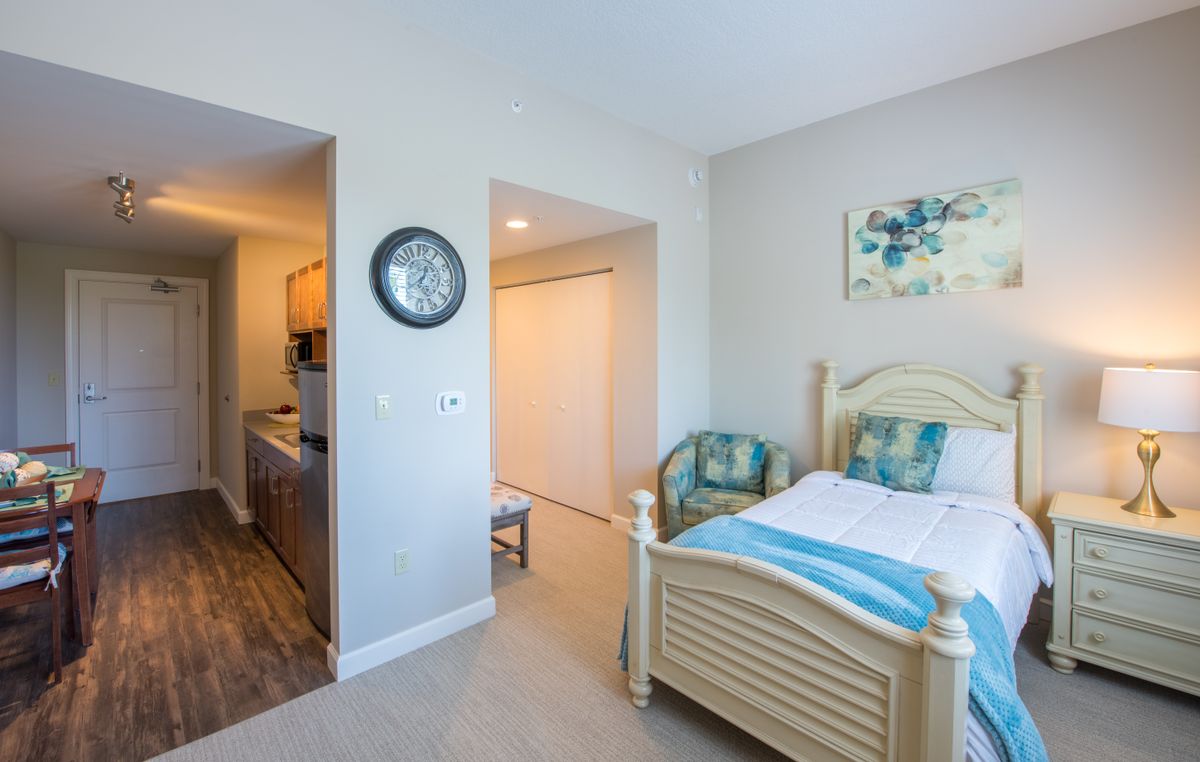 A cozy bedroom with a wooden bed, artwork on the wall, and a clock near the entrance.