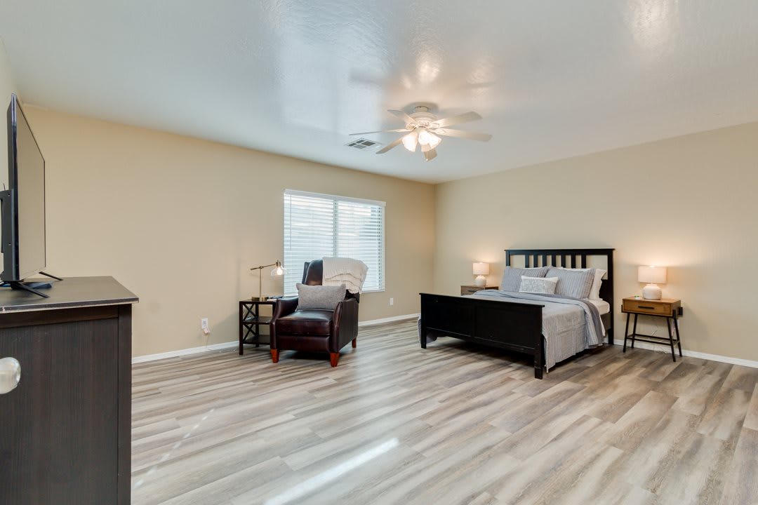 Spacious bedroom with modern decor, featuring a bed, chair, and a large window.