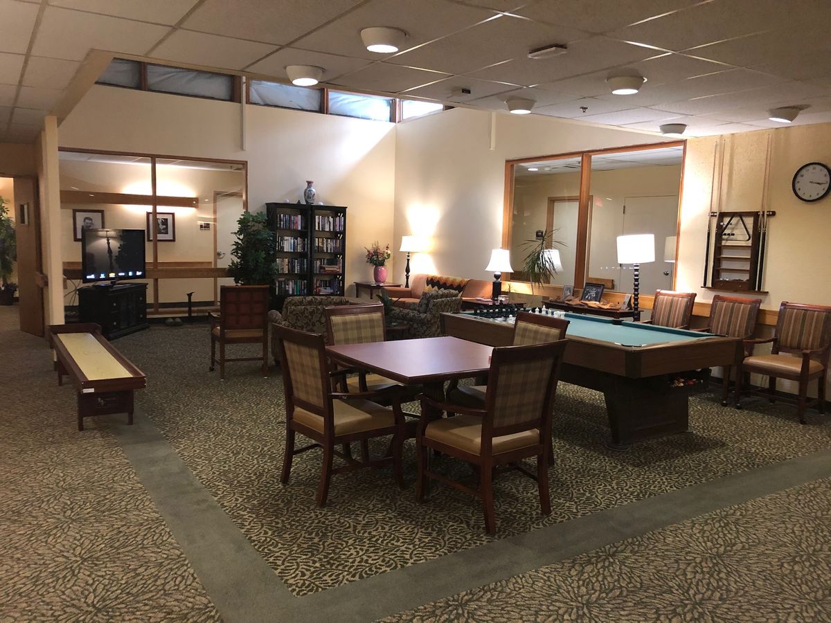 A cozy library interior with tables, chairs, and bookshelves, illuminated by warm lighting.