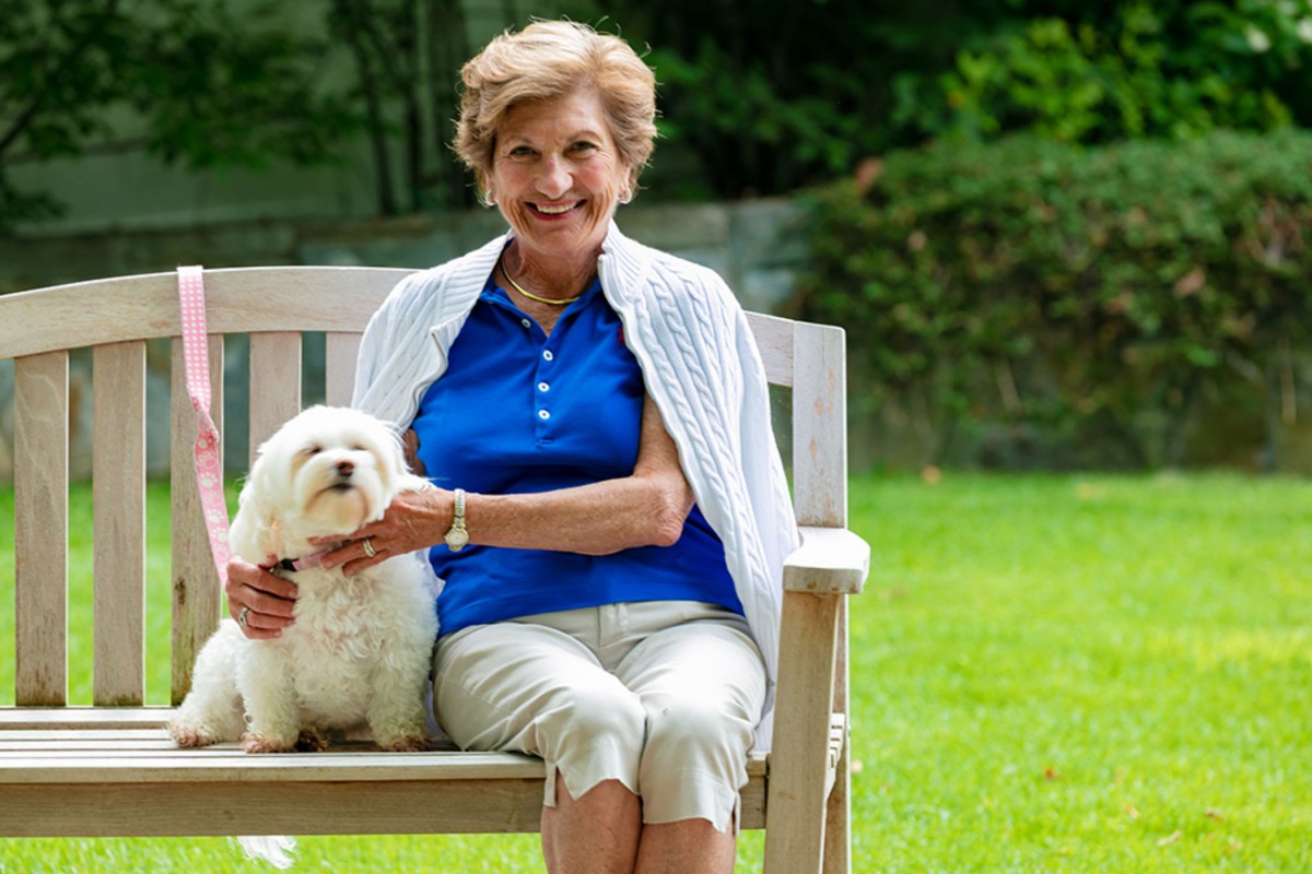 A woman sitting on a bench with her dog in a park.