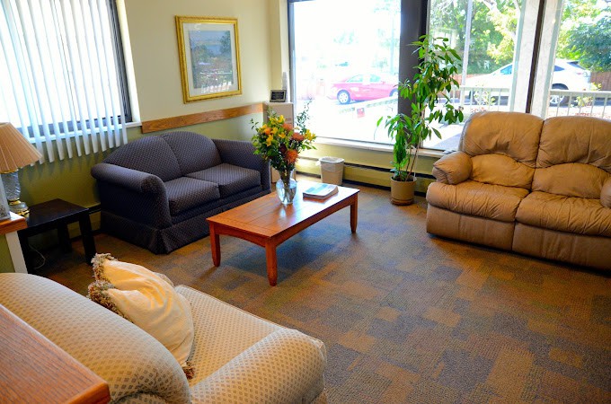 A cozy living room with sofas, an armchair, a coffee table with flowers, and large windows overlooking a view.