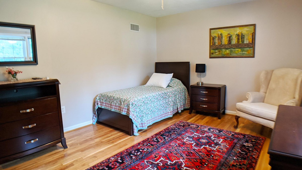 A cozy bedroom with a single bed, nightstand, and colorful rug.