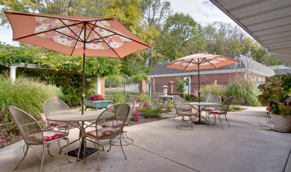 A tranquil patio with tables and chairs under large umbrellas, surrounded by lush greenery.
