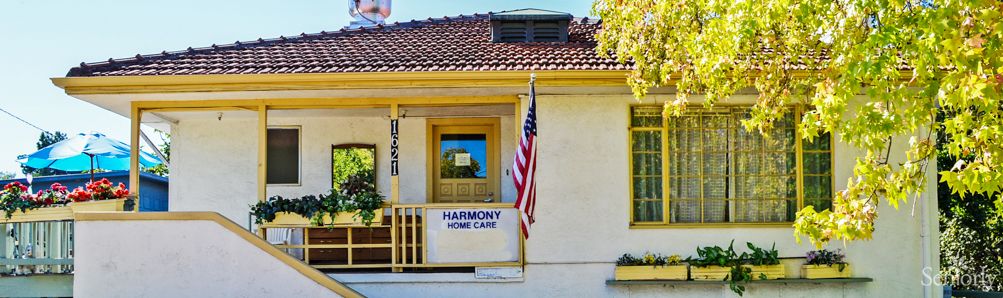 A house with a porch displaying a 'Harmony Home Care' banner and an American flag.