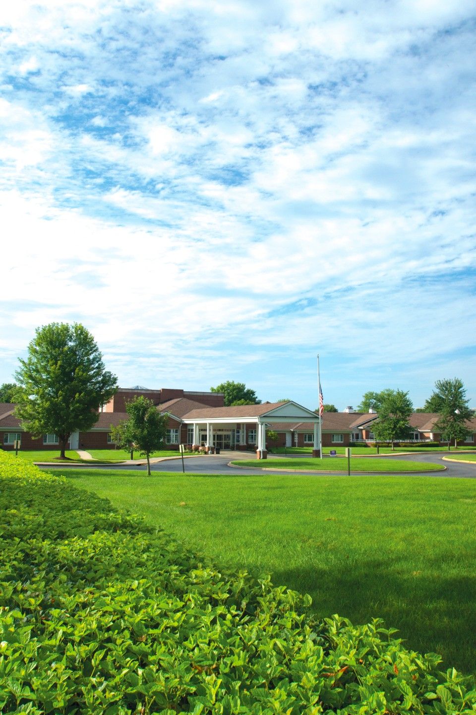 A spacious building surrounded by a large green lawn and trees under a partly cloudy sky.