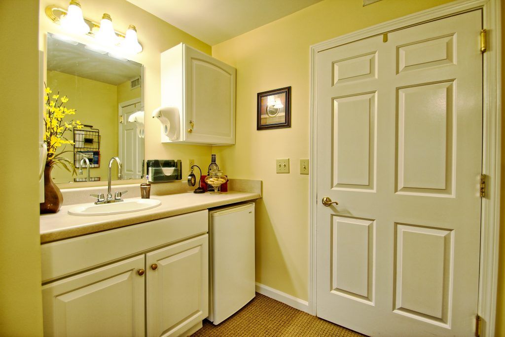 A cozy bathroom with a sink, mirror, and cabinetry against yellow walls.