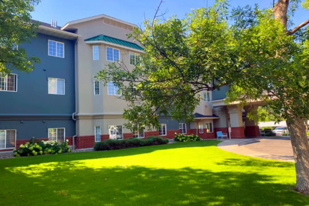 A sunny day view of a residential apartment building with a well-maintained lawn and trees.