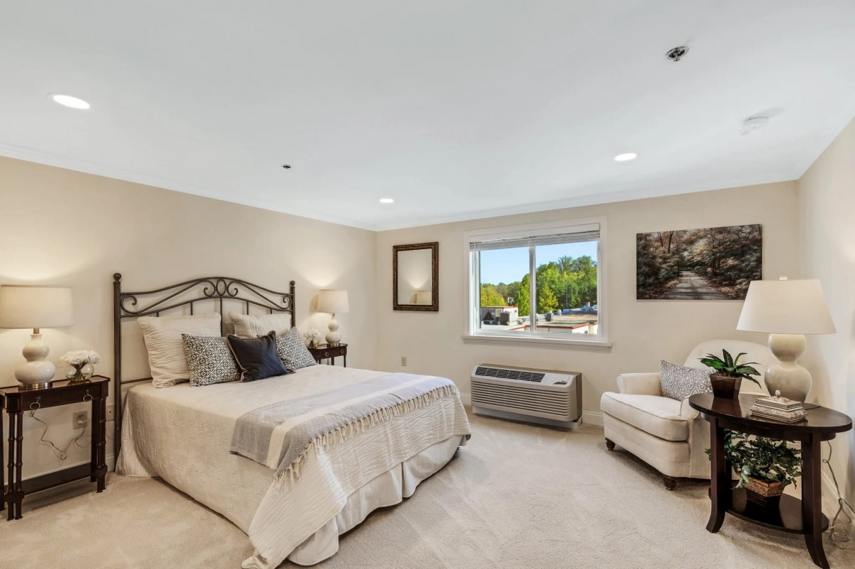 A cozy bedroom with a comfortable bed, armchair, and window view.