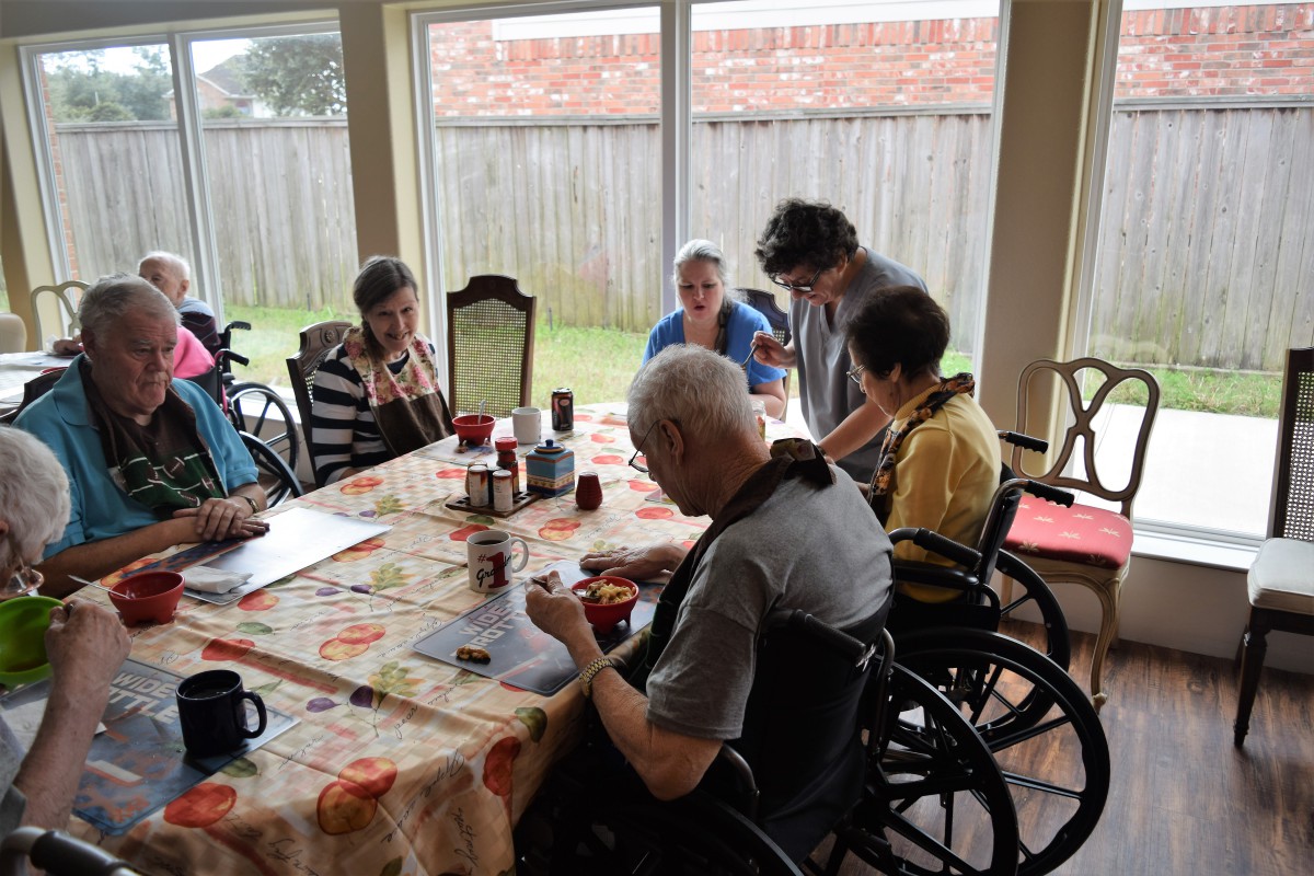 A group of elderly individuals gathered around a table in a care home setting.