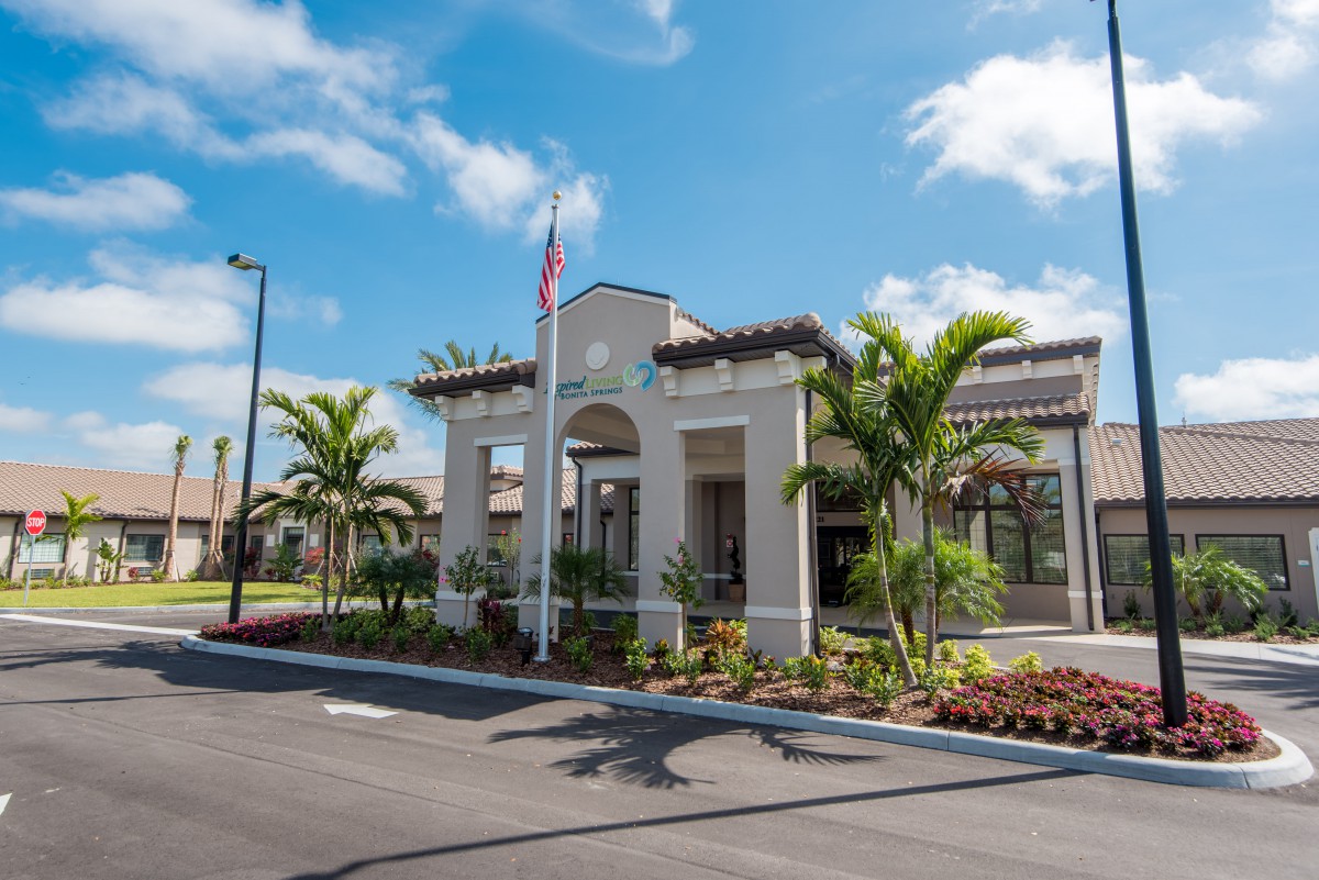A view of a modern building with palm trees and well-maintained landscaping under a blue sky.