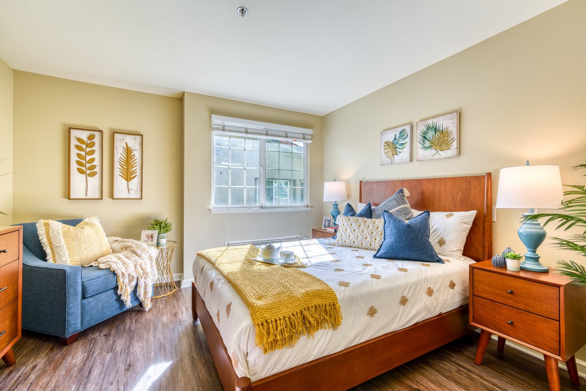 A cozy and bright bedroom featuring a neatly made bed with colorful pillows and a throw blanket, complemented by tasteful decor and ample natural light.