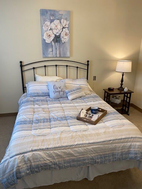 A cozy bedroom with a neatly made bed, decorative pillows, and a bedside lamp.