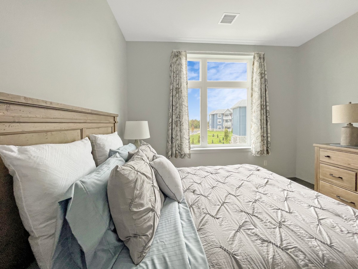 A cozy bedroom with a neatly made bed and sunlight streaming through the window.
