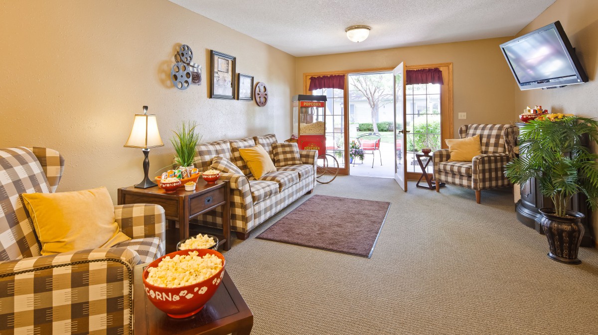 A cozy living room with plaid sofas, a bowl of popcorn on the table, and an inviting open doorway to the outside.