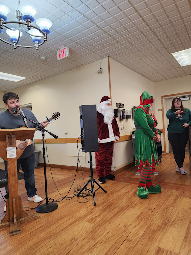 A festive gathering featuring musical performances, with Santa Claus and an elf on stage.