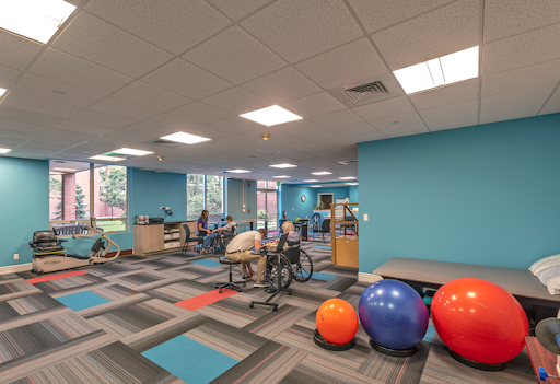 A bright and spacious rehabilitation gym featuring various exercise equipment and colorful fitness balls.