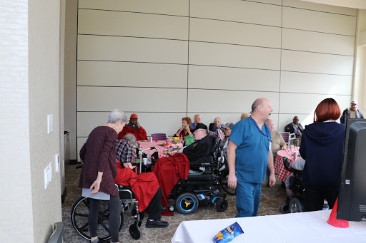 A lively community event with elderly individuals gathered together, some in wheelchairs, enjoying their time indoors.
