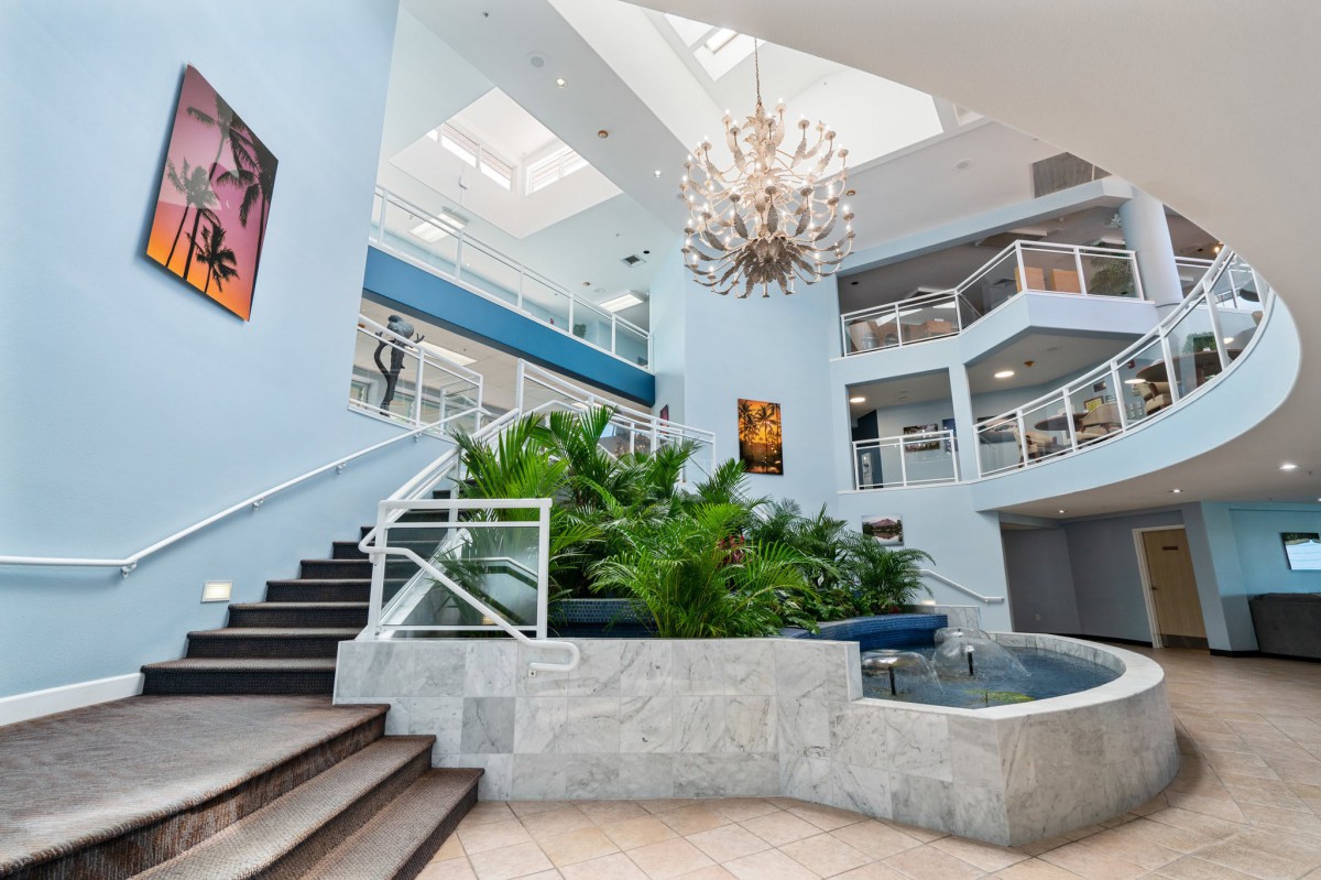 A modern atrium featuring a grand staircase, elegant chandelier, and lush indoor plants.