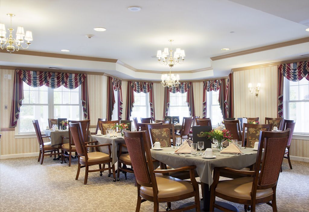 A well-lit dining area with elegant chandeliers, decorated windows, and neatly arranged tables and chairs.