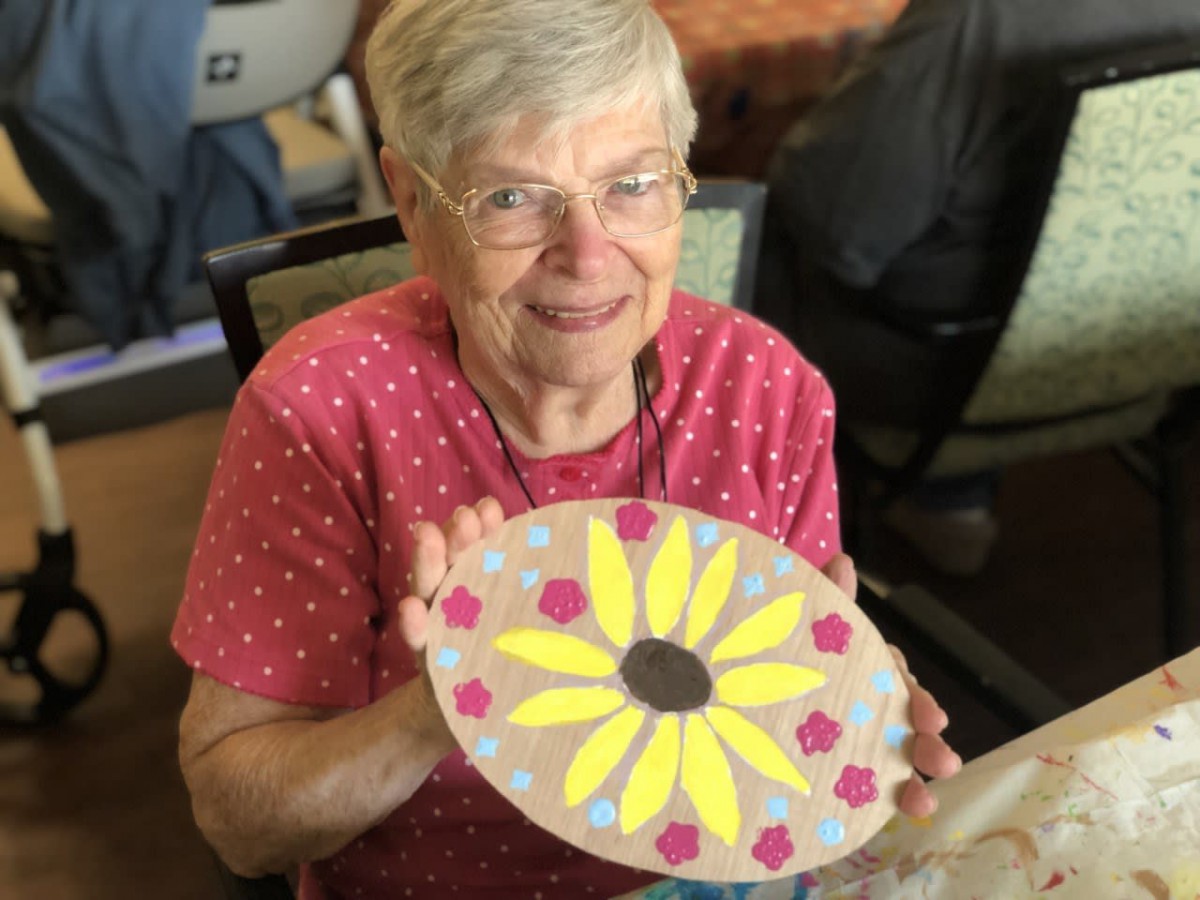 An elderly woman proudly displays her handmade flower craft.