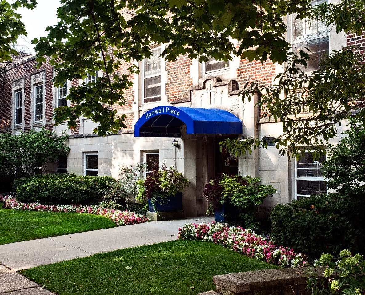 A charming building entrance with a blue awning, surrounded by well-maintained landscaping and vibrant flowers.