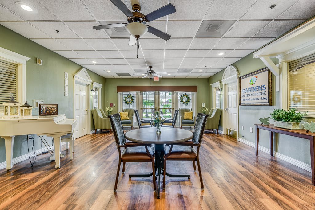 A spacious dining area with wooden floors, tables and chairs, illuminated by natural light and featuring ceiling fans for ventilation.